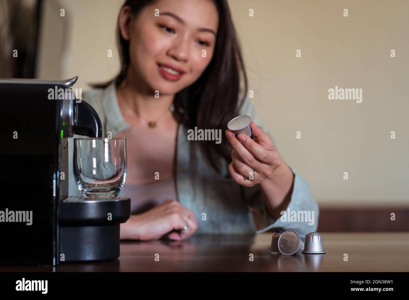 Raccolto sorridente giovane etnia femmina mettere cialda di caffè in macchina sul tavolo in cucina casa Foto Stock