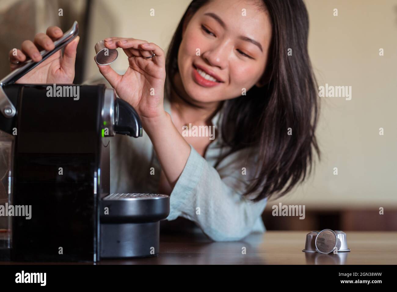 Raccolto sorridente giovane etnia femmina mettere cialda di caffè in macchina sul tavolo in cucina casa Foto Stock
