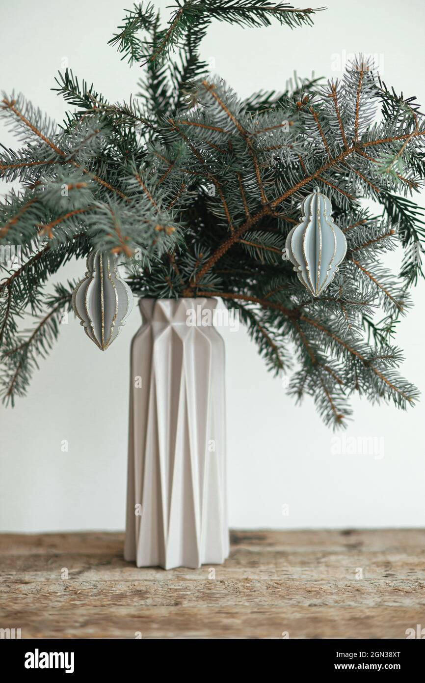 Elegante ornamento di natale su ramo di abete in vaso moderno primo piano. Moderno bauble in legno su ramo su sfondo bianco. Decorazioni semplici e creative per le feste Foto Stock