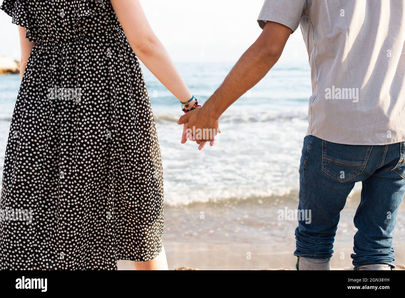 Coppia interrazziale che tiene le mani di fronte al mare Foto Stock