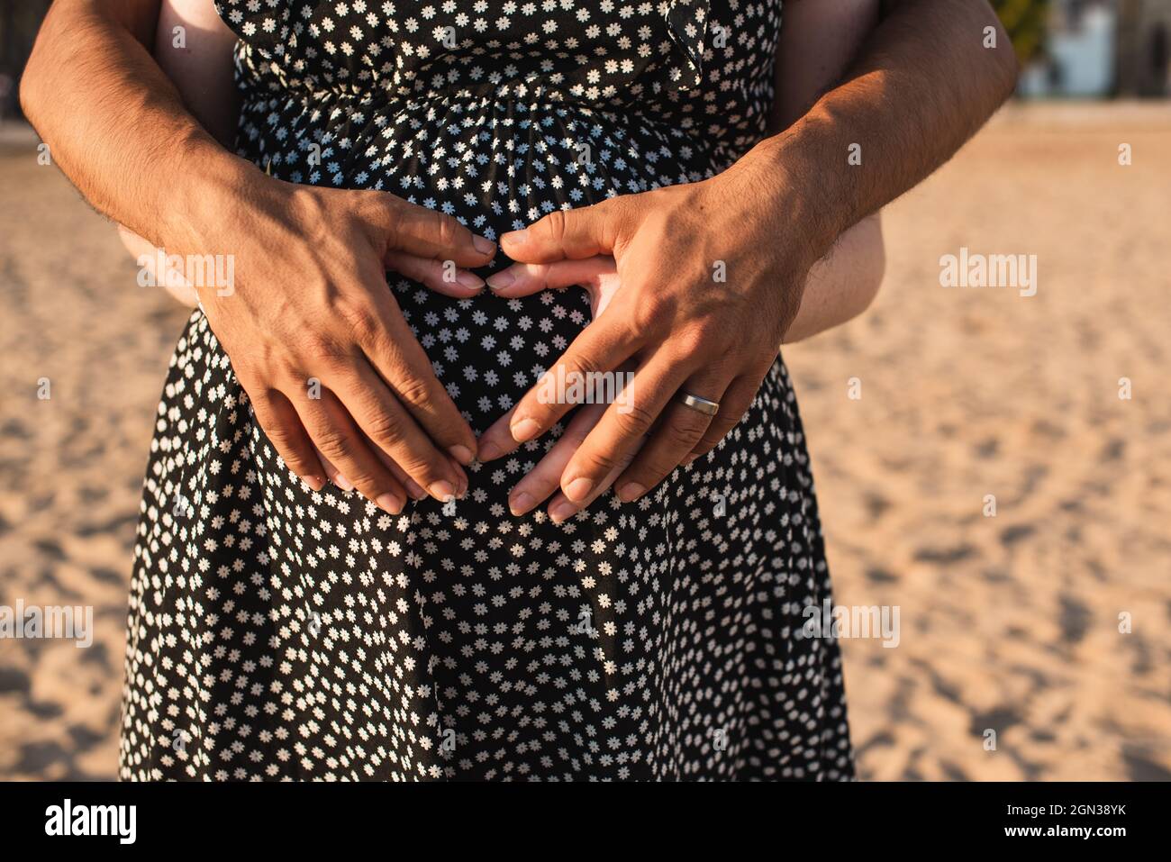 Coppia interrazziale in attesa di un bambino. Cuore con le mani sul ventre della donna incinta. Foto Stock