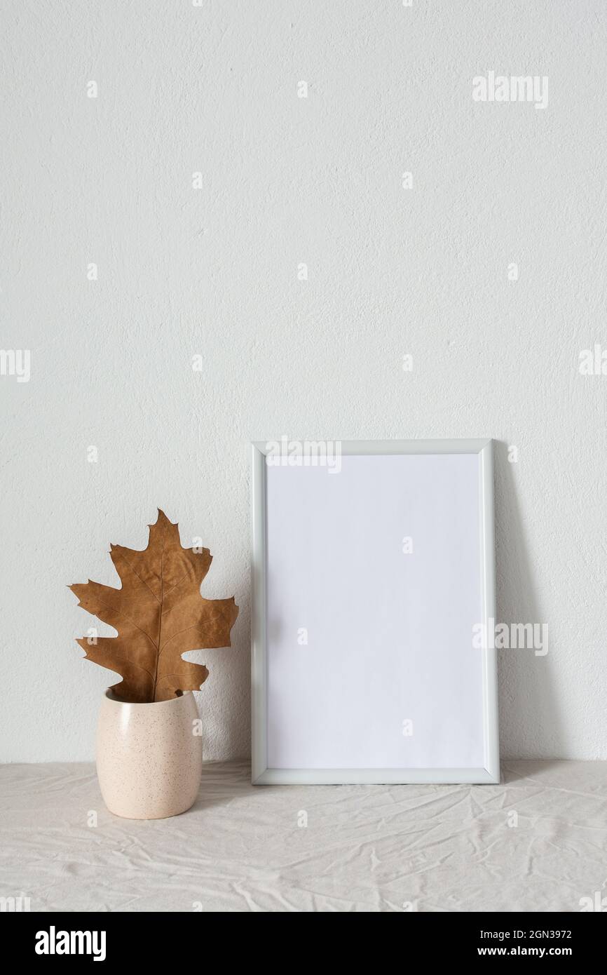 Casa decoratore moccap, quadro vuoto cornice vicino bianco dipinto muro di cemento, rami con foglie asciutte Foto Stock