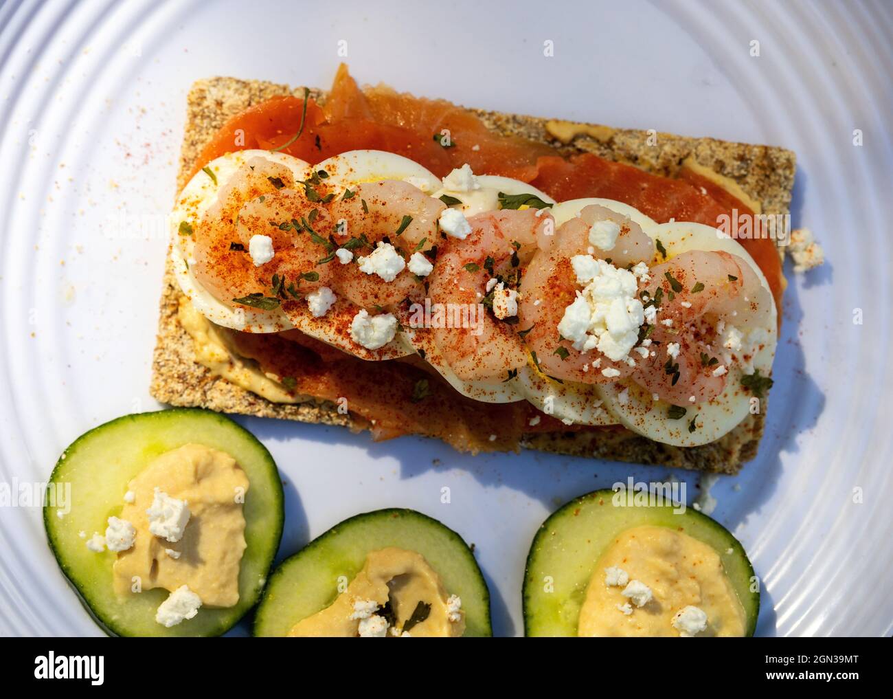 Sandwich aperto in stile scandinavo Rye pane croccante salmone affumicato affumicato uovo sode gamberetti Feta formaggio e paprika cetrioli fette con Hummus Foto Stock