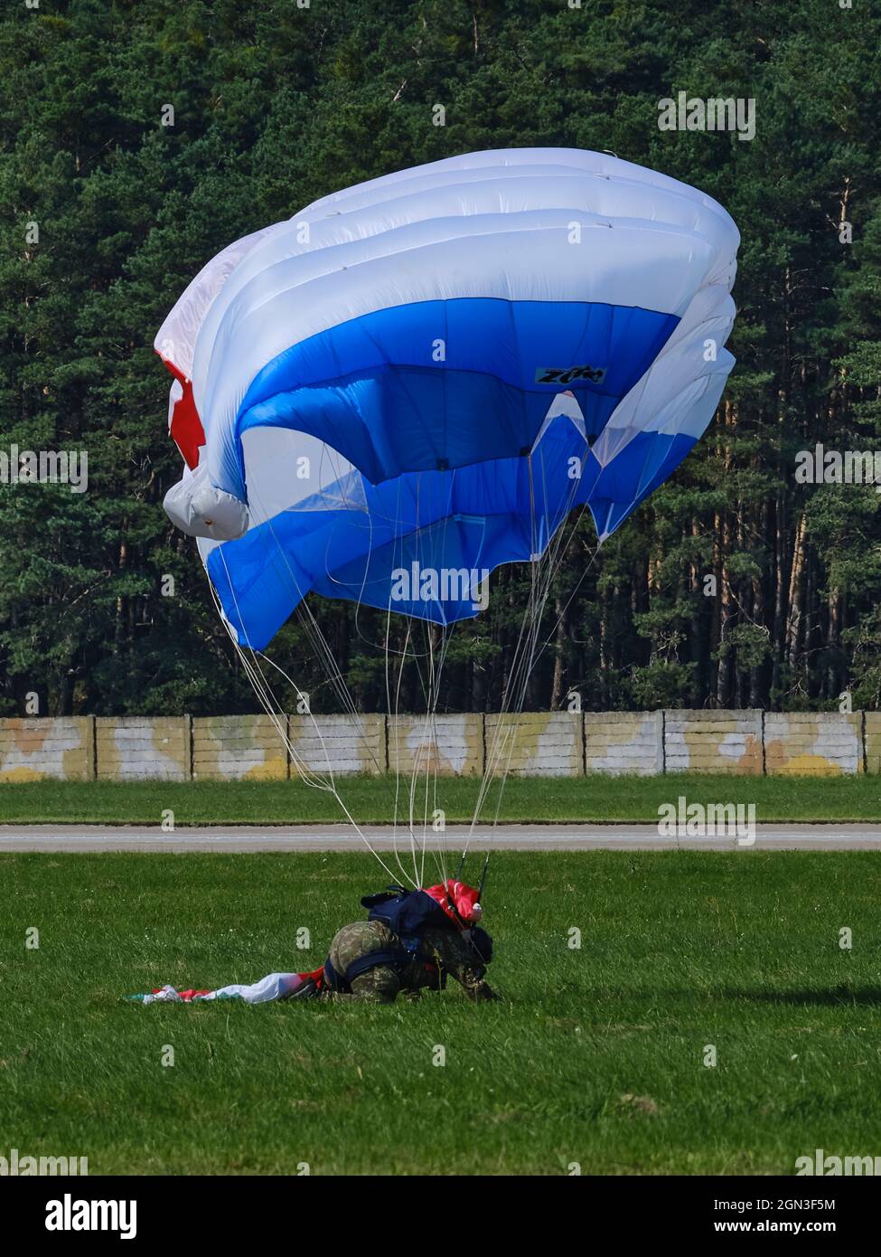 Il paracadutista atterra su un campo d'aviazione in erba con un baldacchino blu e bianco durante un'esibizione aeronautica. Foto Stock