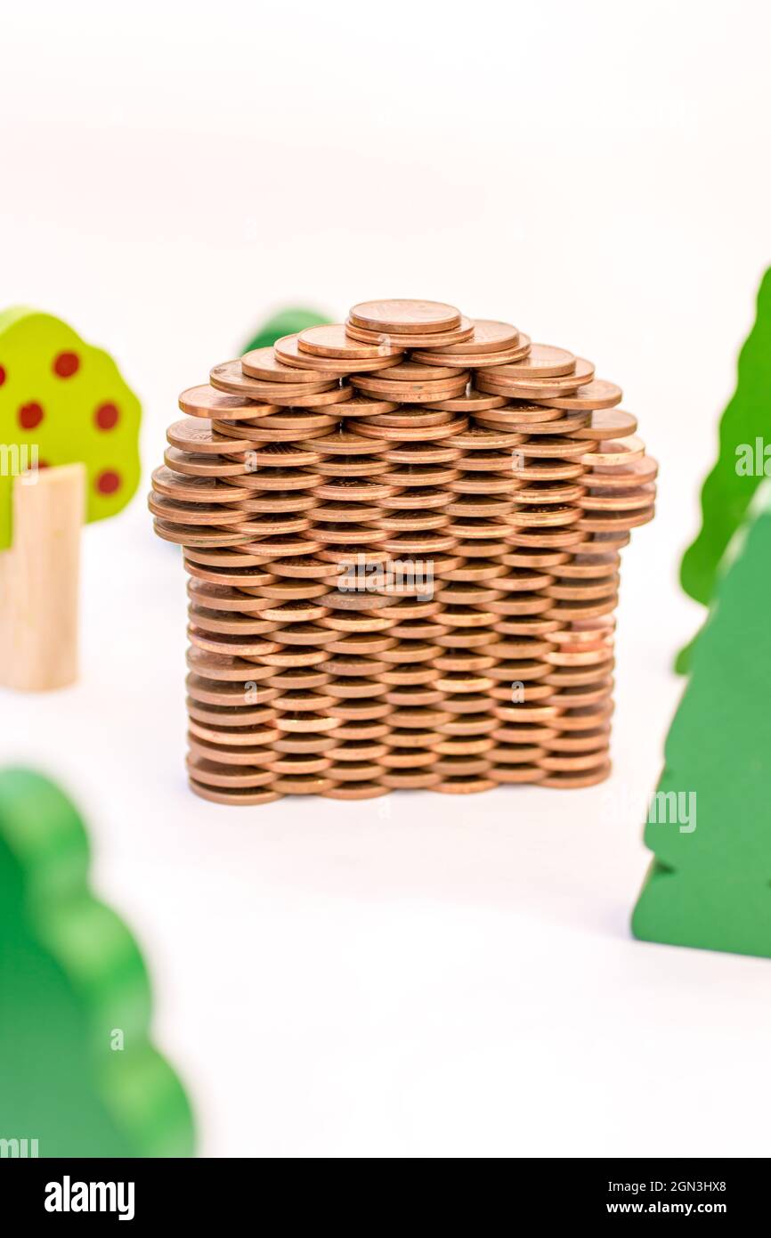 Casa fatta di monete tra gli alberi come simbolo di costo da costruzione casa Foto Stock
