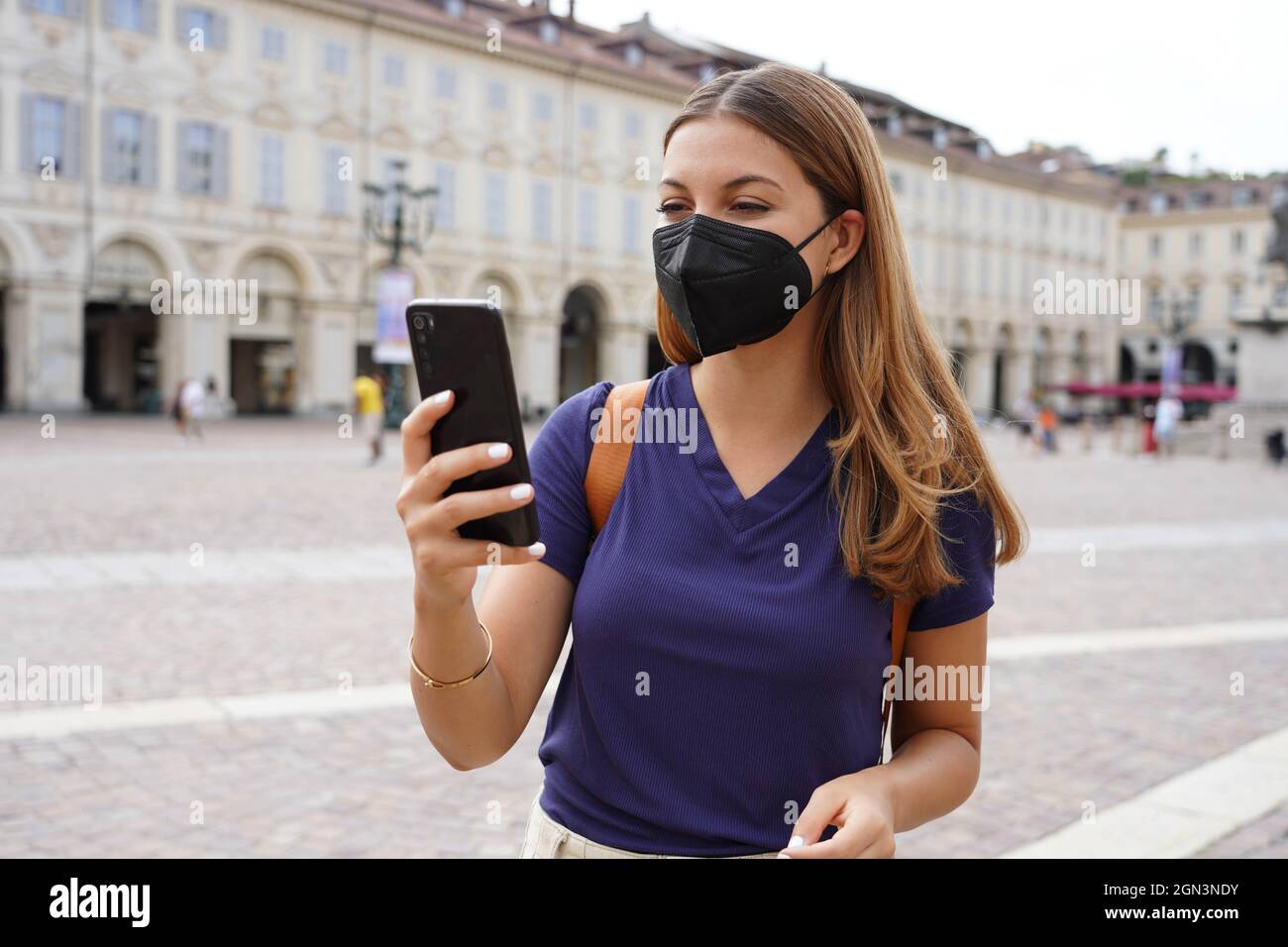 Ritratto della studentessa con maschera protettiva nera FFP2 KN95 con smartphone all'aperto Foto Stock