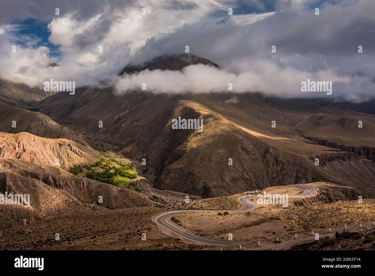 Piccolo campo di coltura verde nel mezzo delle montagne deserte, e una strada di montagna piena di giri a Jujuy, Argentina Foto Stock