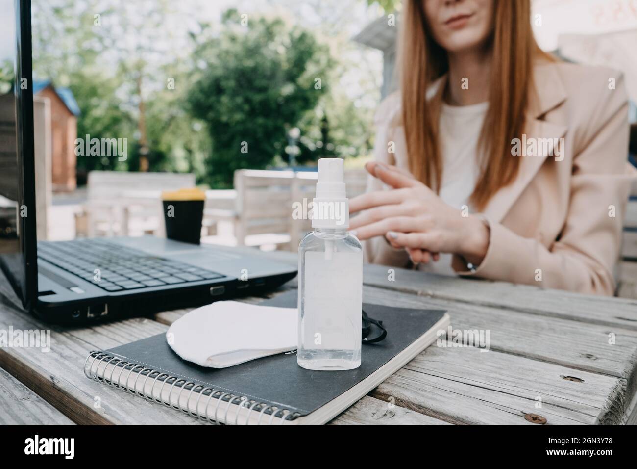 Donna d'affari rossa che usa il gel antisettico per disinfettare le mani sopra una scrivania in un posto di lavoro esterno. Misure preventive durante il periodo di Foto Stock