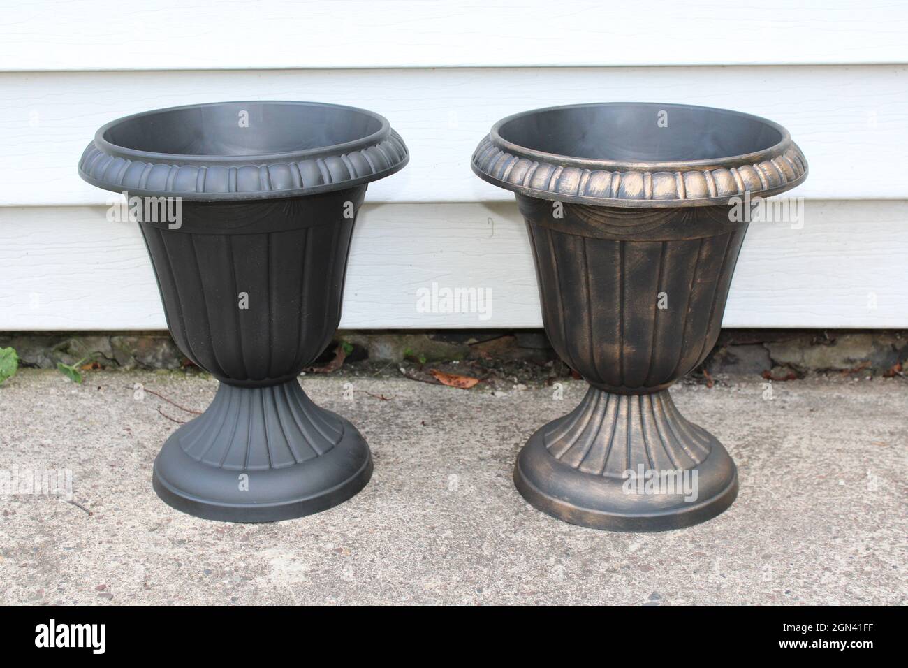 Una piantatrice di plastica nera non verniciata accanto ad una piantatrice di plastica nera verniciata di rame Foto Stock