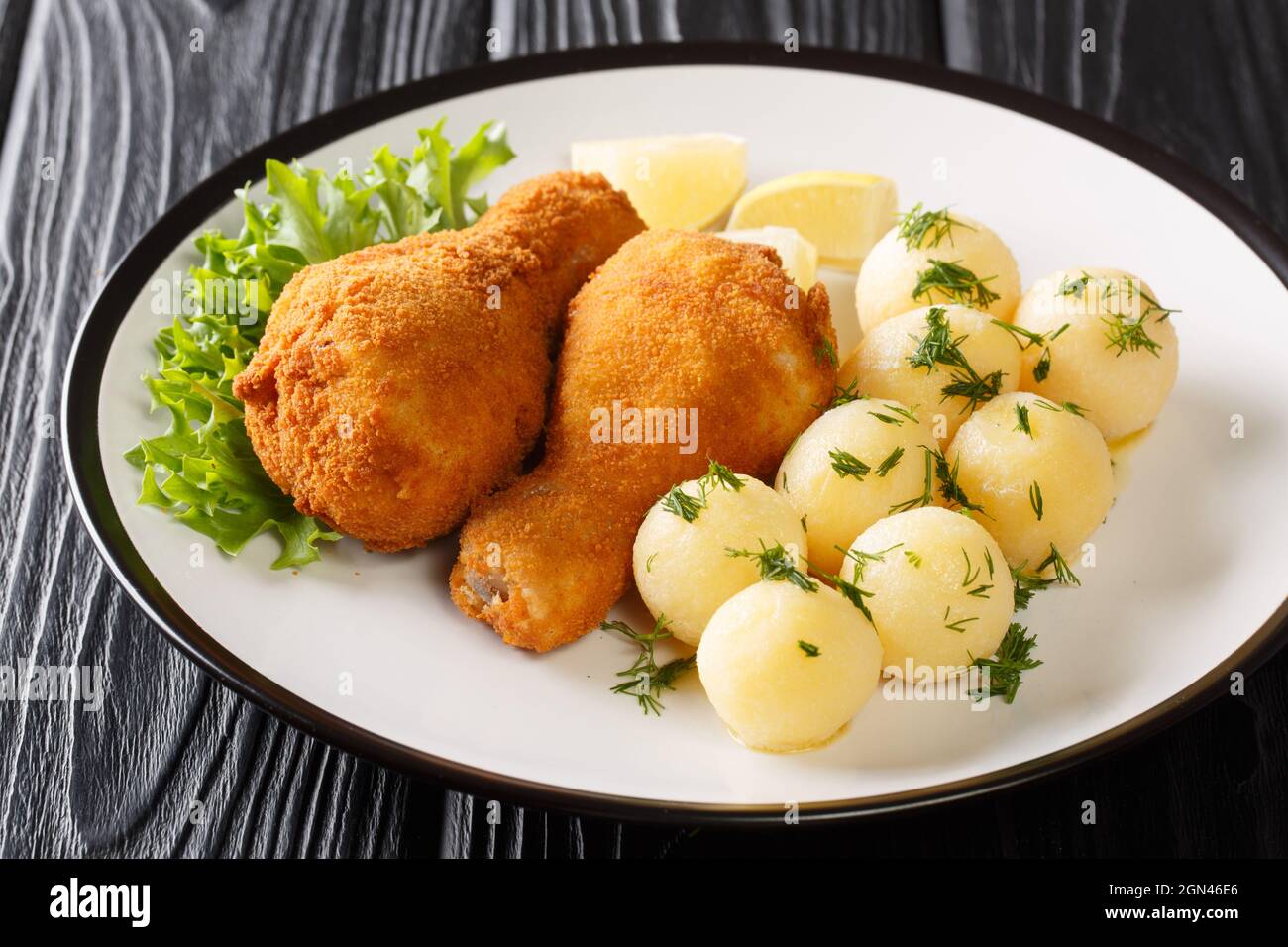 Pollo impanato austriaco fritto e servito con limone e patate novelle primo piano su un piatto sul tavolo. Orizzontale Foto Stock