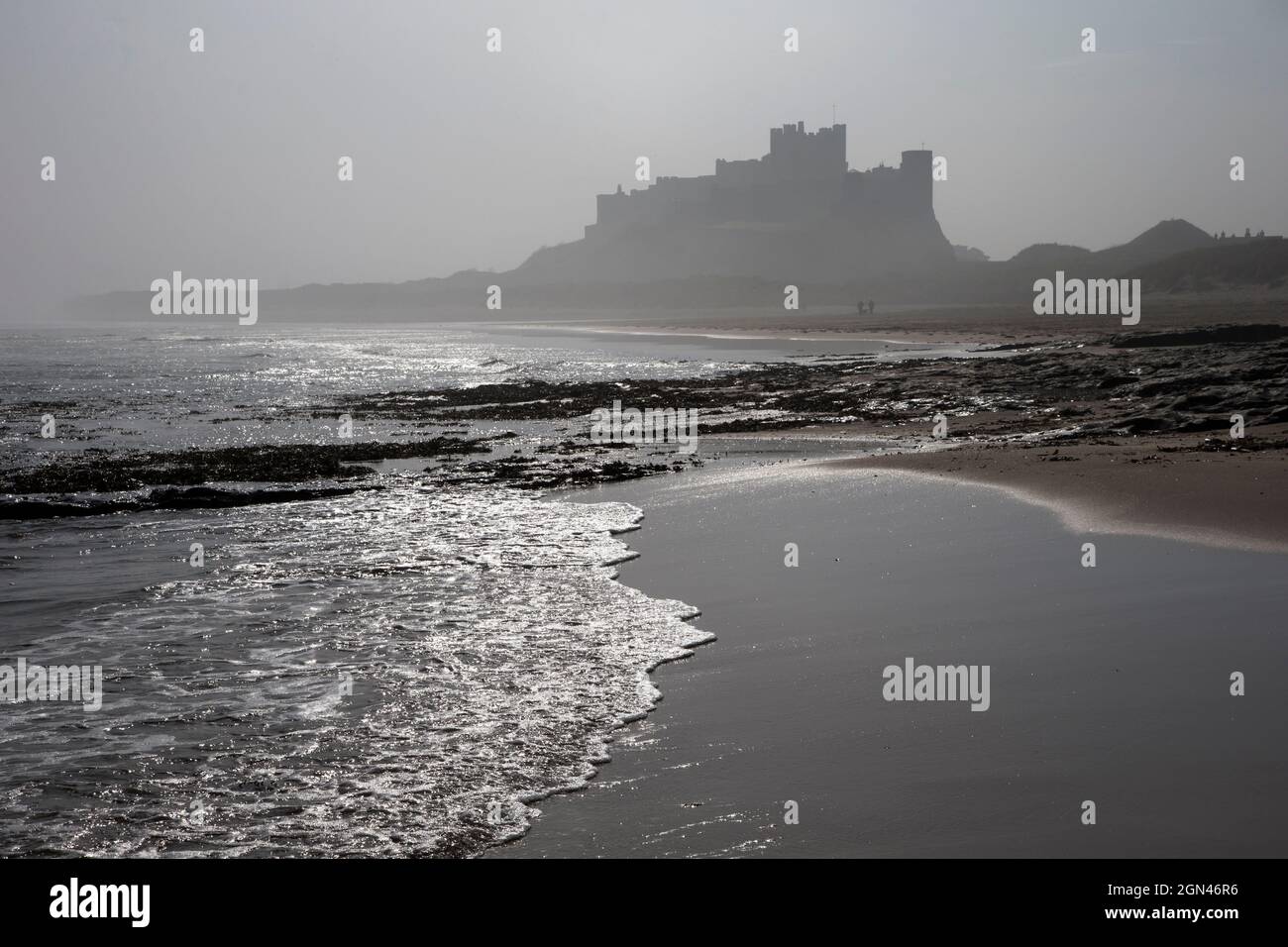 Onde che si infrangono a Bambburgh Beach guardando verso il Castello di Bambburgh in una mattinata di nebbia, Northumberland, Regno Unito, Foto Stock