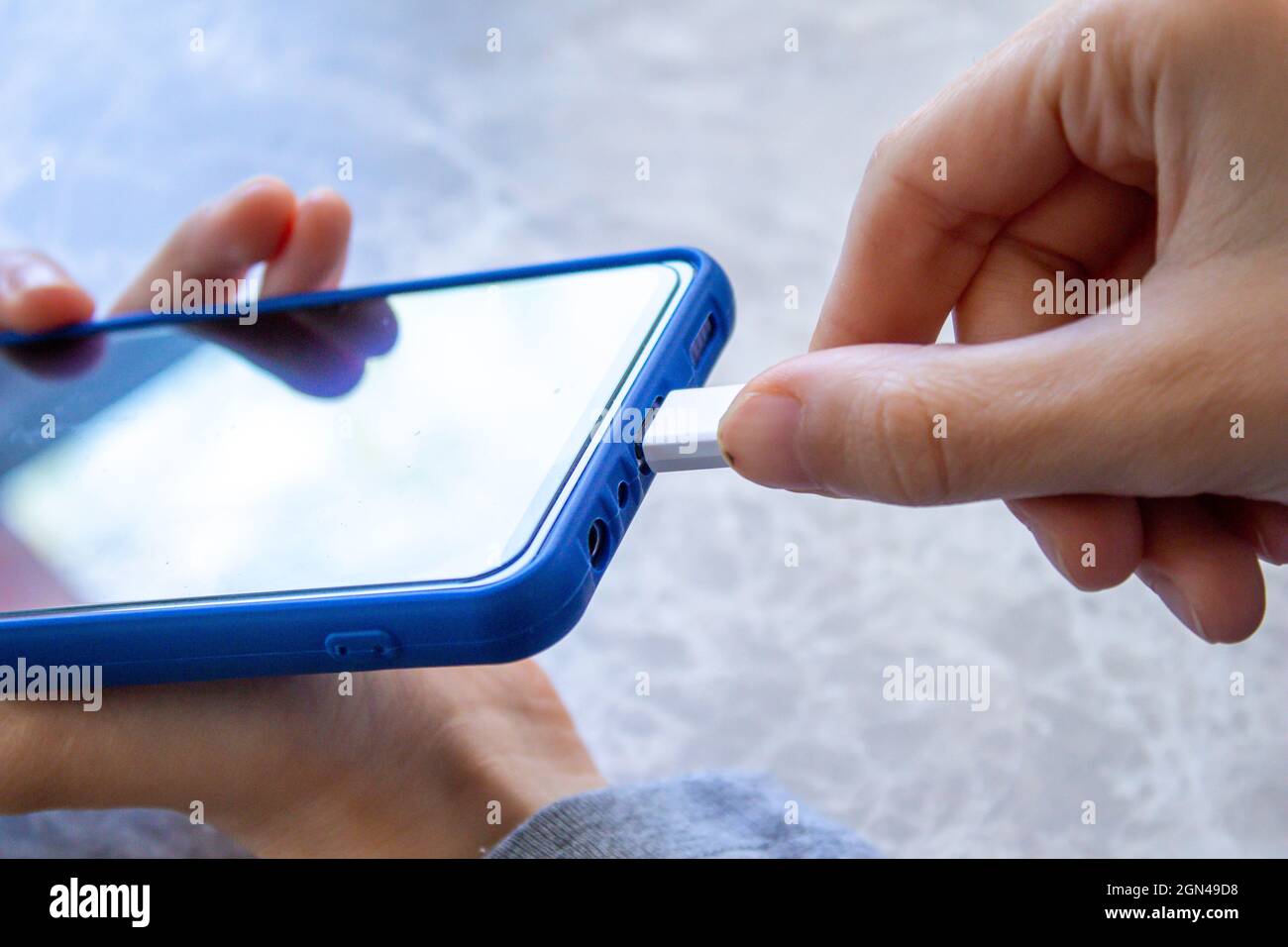 La giovane donna collega il telefono al caricabatterie. Foto Stock