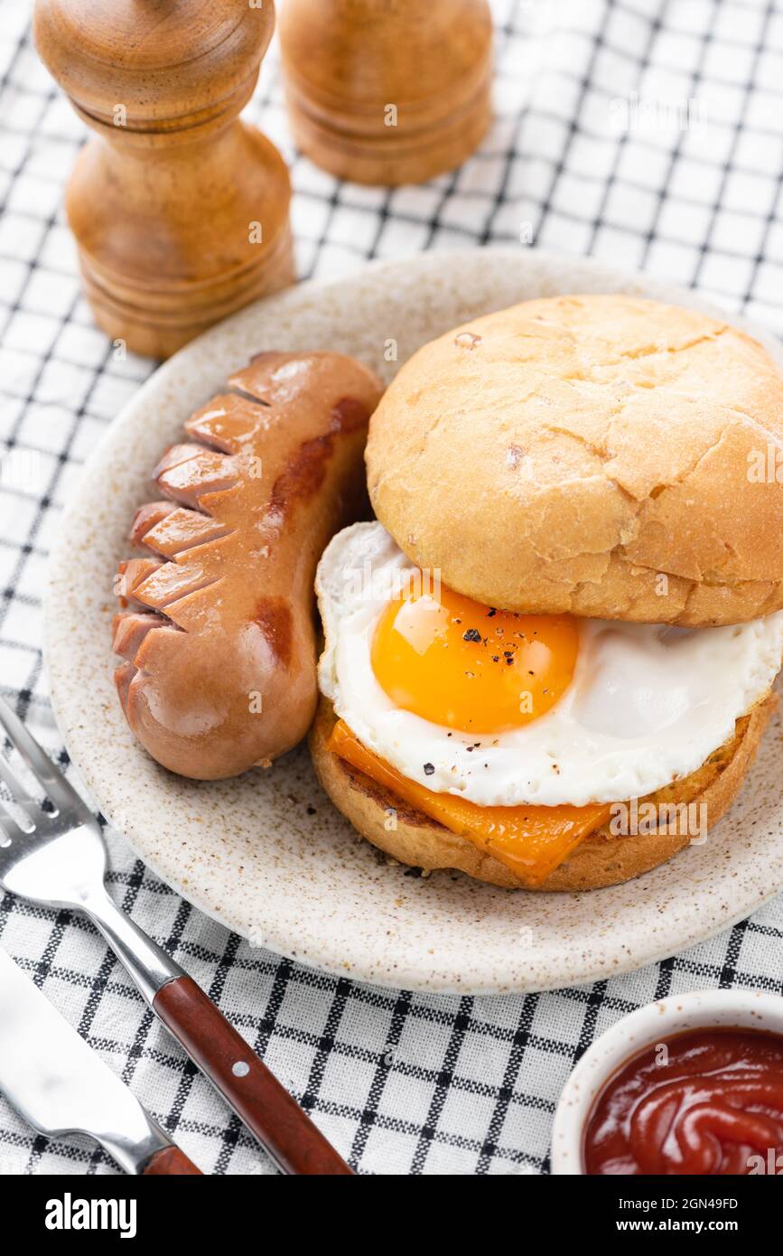 Sandwich per la colazione con uova fritte, formaggio, salsiccia su un piatto. Colazione o pranzo servito in caffetteria, ristorante Foto Stock