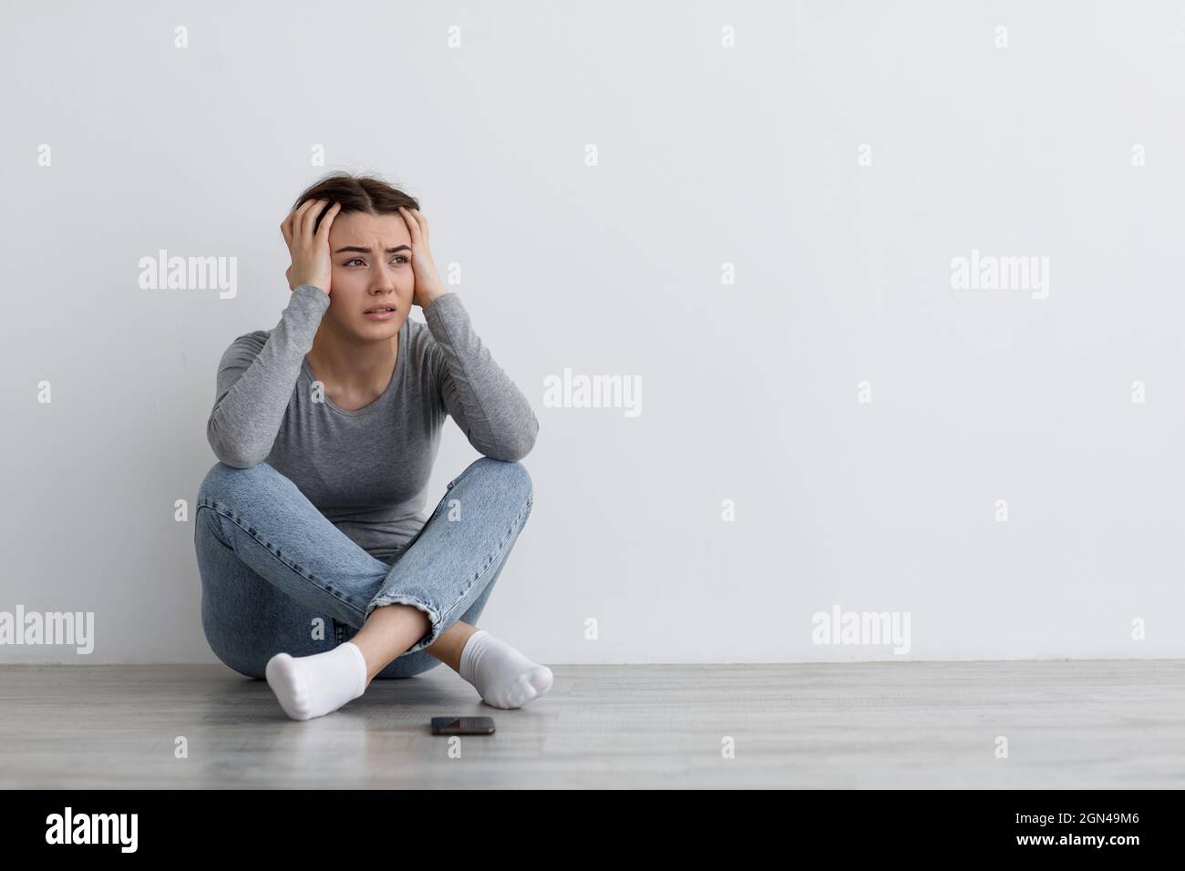 Disperazione ansiosa signora millenaria caucasica seduta a terra, soffrendo di depressione, preoccupato e ricevuto cattive notizie Foto Stock