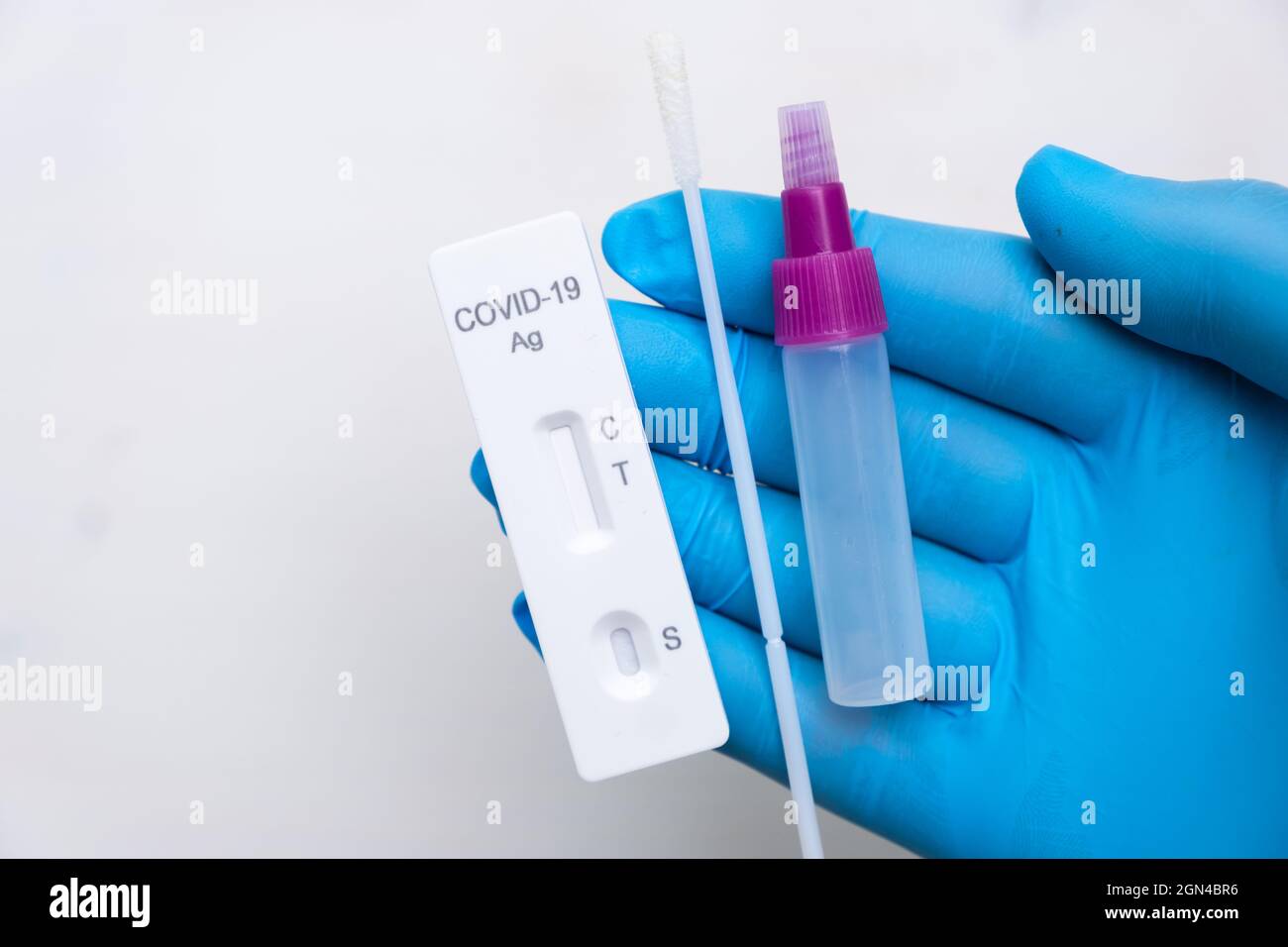Nuovo kit antigenico per il test del coronavirus con bastoncino nasale per diagnostica rapida in mano del medico con guanti di gomma su sfondo bianco Foto Stock