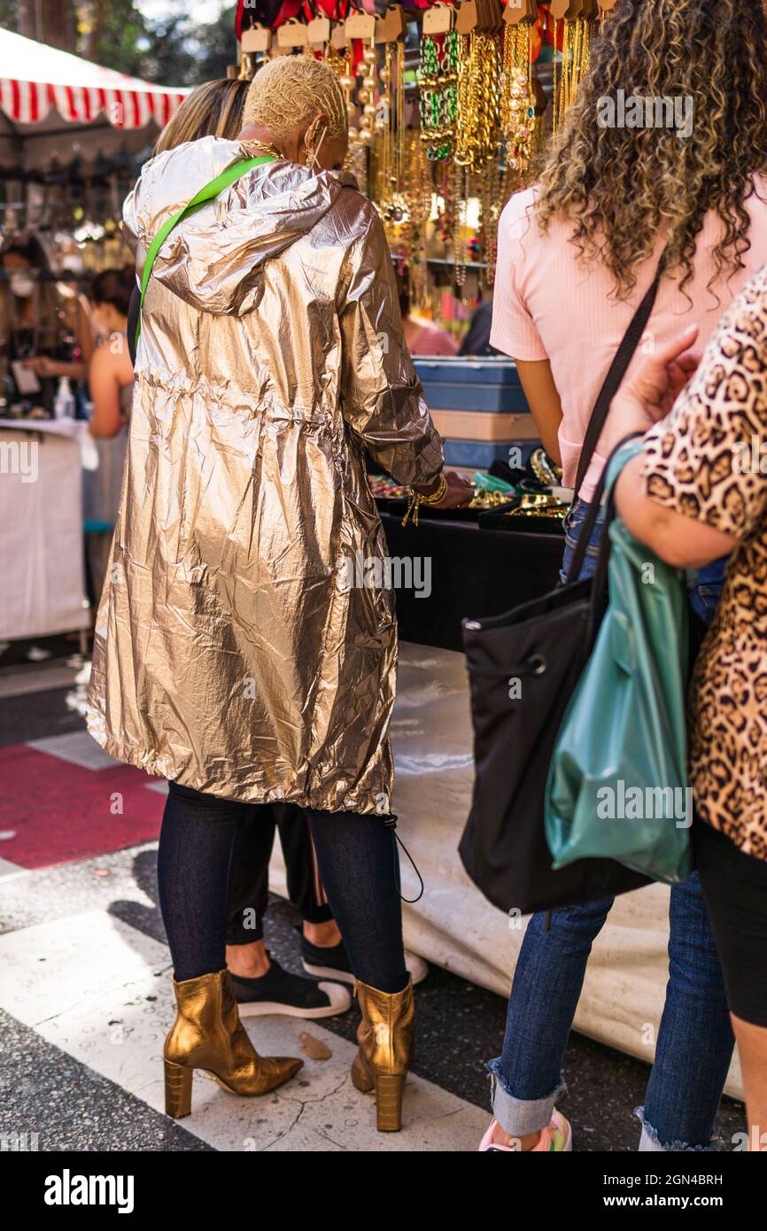Donna che indossa una giacca in oro metallizzato con felpa con cappuccio e altri gioielli in costume da shopping da donna alla fiera Belo Horizonte Hippie in Brasile. Foto Stock