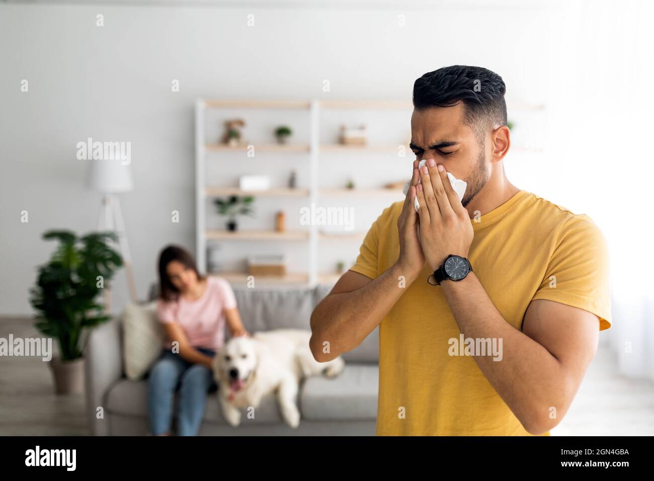 Il giovane ragazzo arabo starnutisce e soffia il naso in carta tissue, ha un cattivo freddo, rimanendo a casa con la sua ragazza e il suo cane Foto Stock