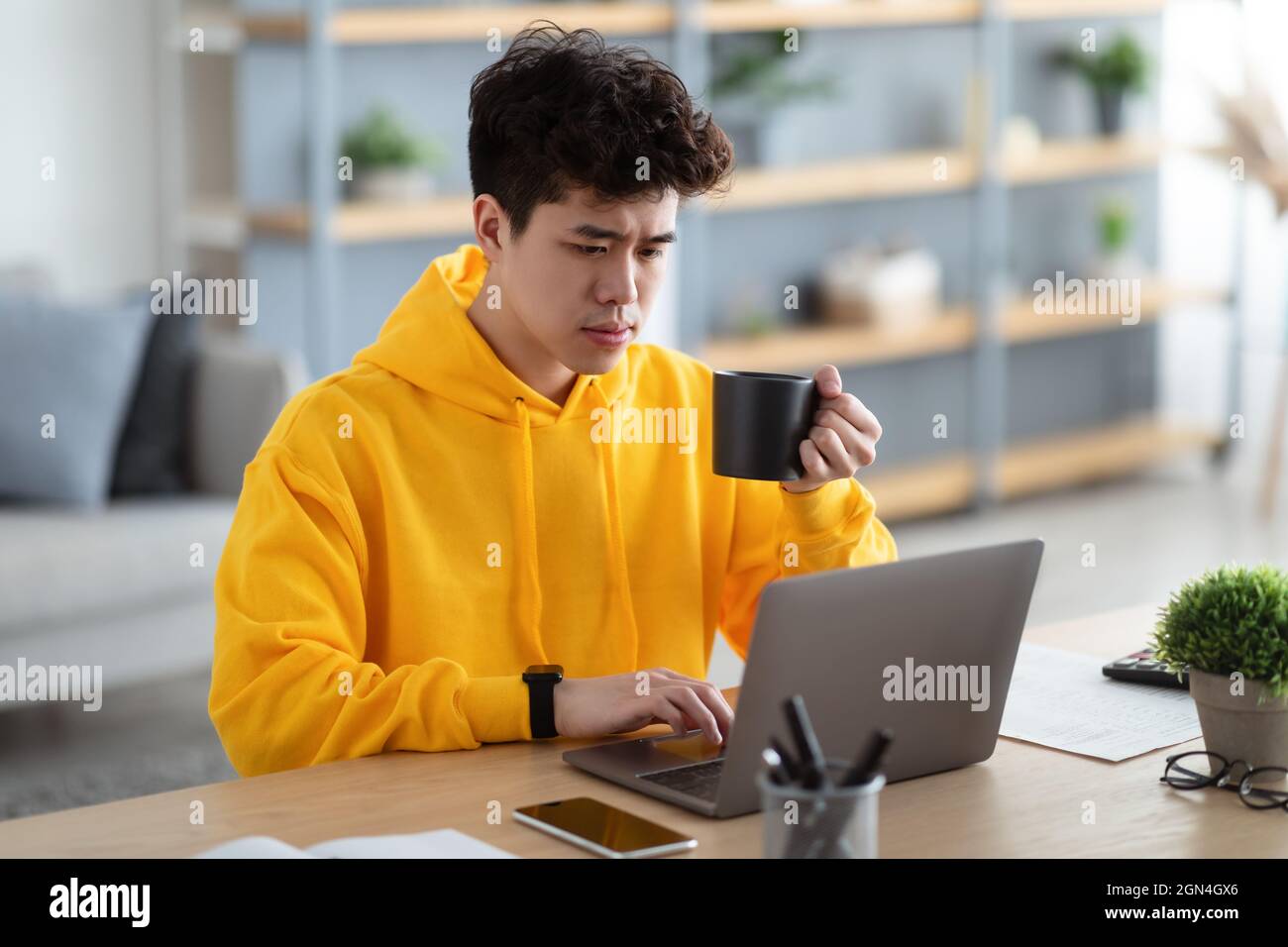 Uomo asiatico serio guardare video su pc, bere caffè caldo Foto Stock
