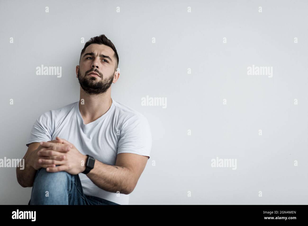 Uomo colpevole depresso seduto contro il muro bianco a casa sensazione infelice, solitario e triste, depressione salute mentale, covid Foto Stock