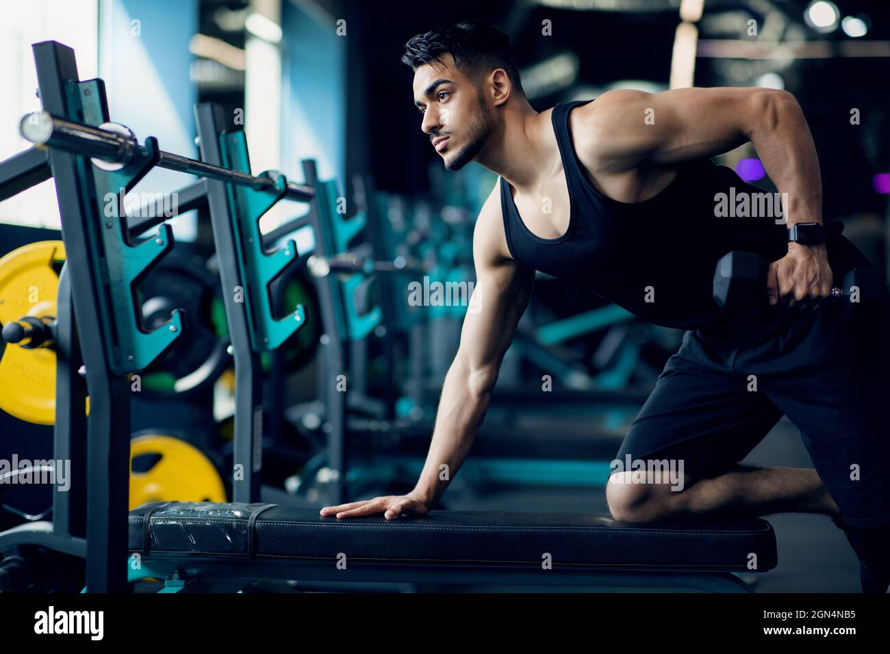 Motivato bell'addestramento dell'uomo arabo con Dumbbell al moderno interno della palestra Foto Stock
