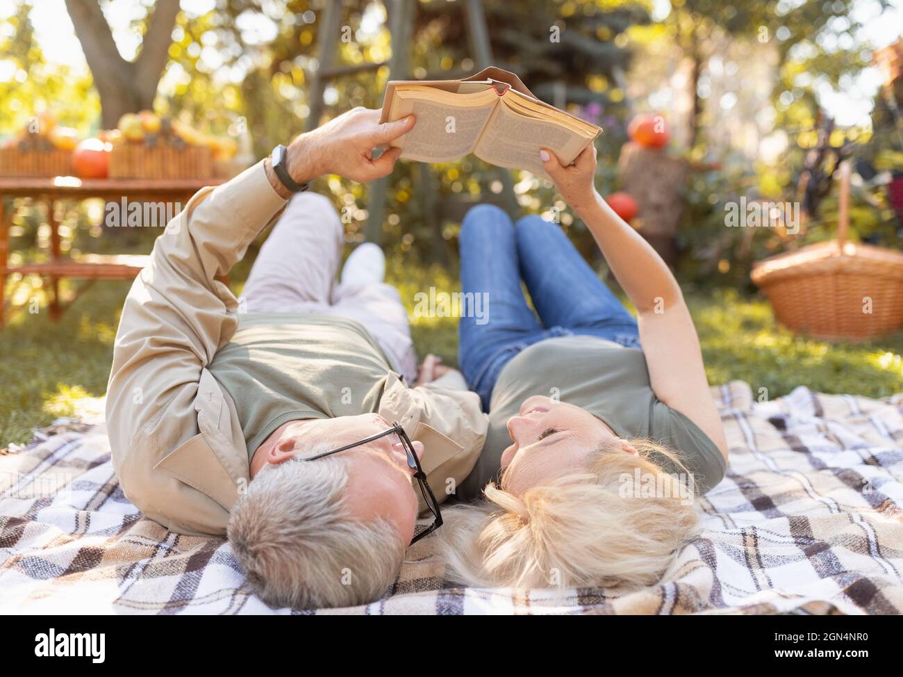 Coppia sposata libro di lettura insieme mentre si trova su coperta da picnic in giardino, trascorrere il tempo libero all'aperto Foto Stock