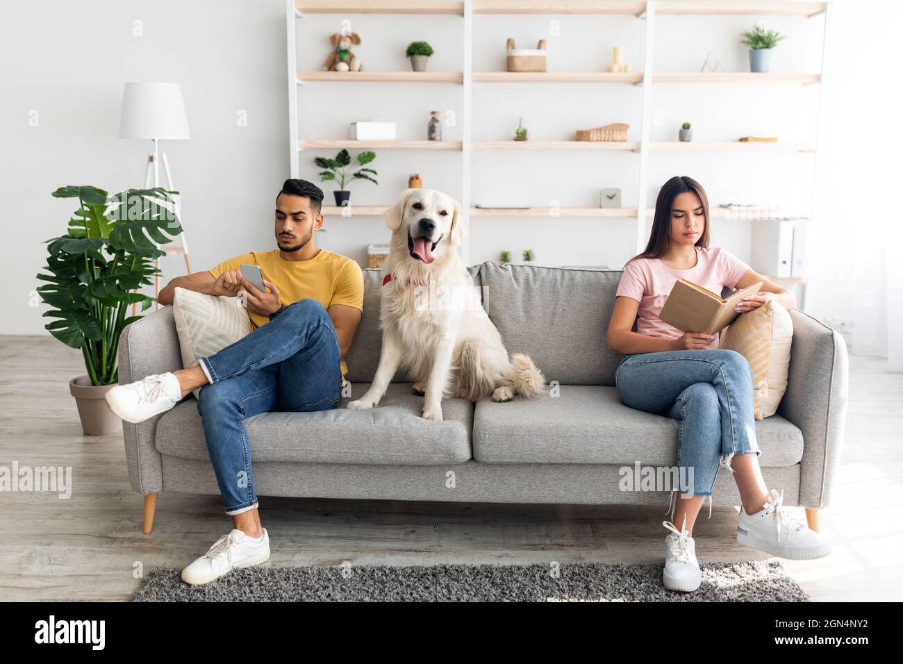 Giovane coppia inerraciale in conflitto, seduta su lati opposti del divano a casa, cane tra loro Foto Stock