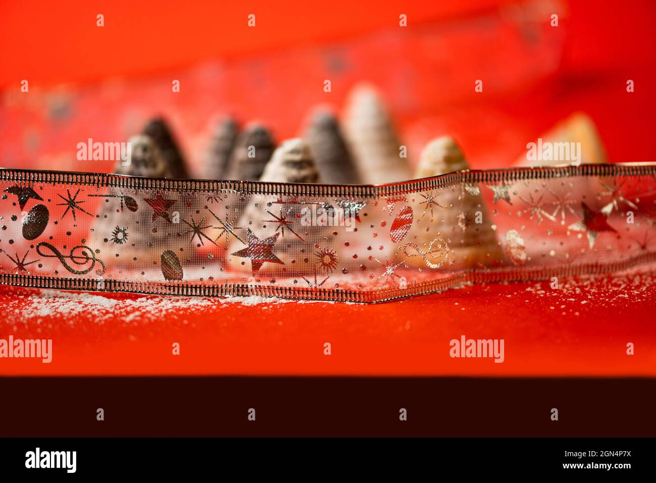 Gruppo sfocato di torta di alveare di natale dietro nastro ornamentale su sfondo rosso bello festivo. Sfondo allegro quasi astratto. Foto Stock
