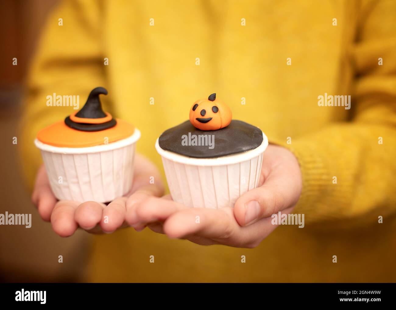 Un bambino sta tenendo i muffin di Halloween con le decorazioni nella forma di una zucca e di un cappello della strega. Set di cupcakes per le vacanze e dolcetti di Halloween. Foto Stock