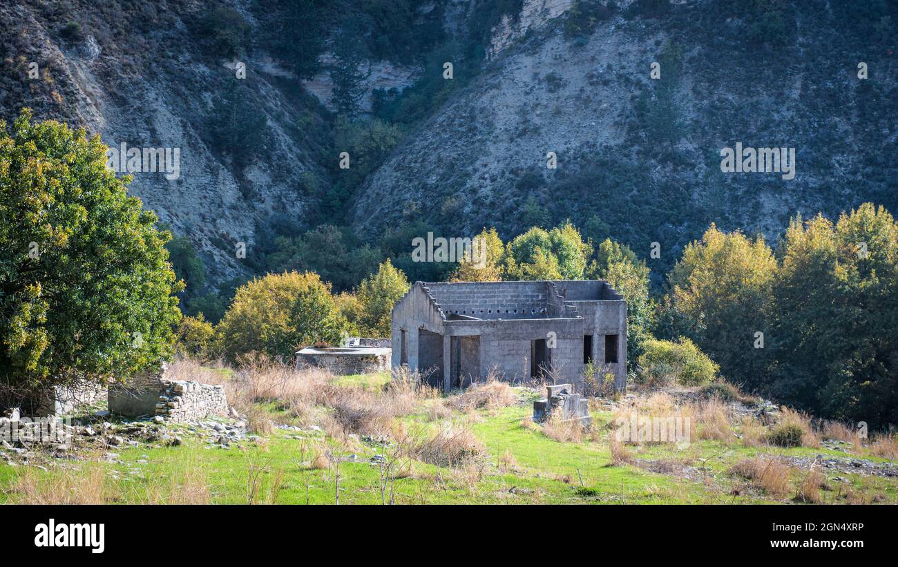 Rovine di casa in pietra senza tetto e giardino in sovrappiente ai piedi di una montagna. Paesaggio abbandonato villaggio Foto Stock