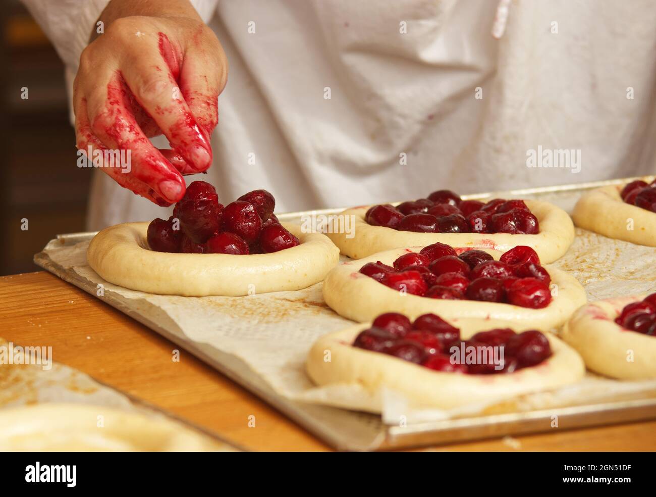 La donna nella foto sta facendo torte di frutta riempite. Mani che riempiono la pasta di lievito con fragole. Lavoro nel panificio. Foto Stock