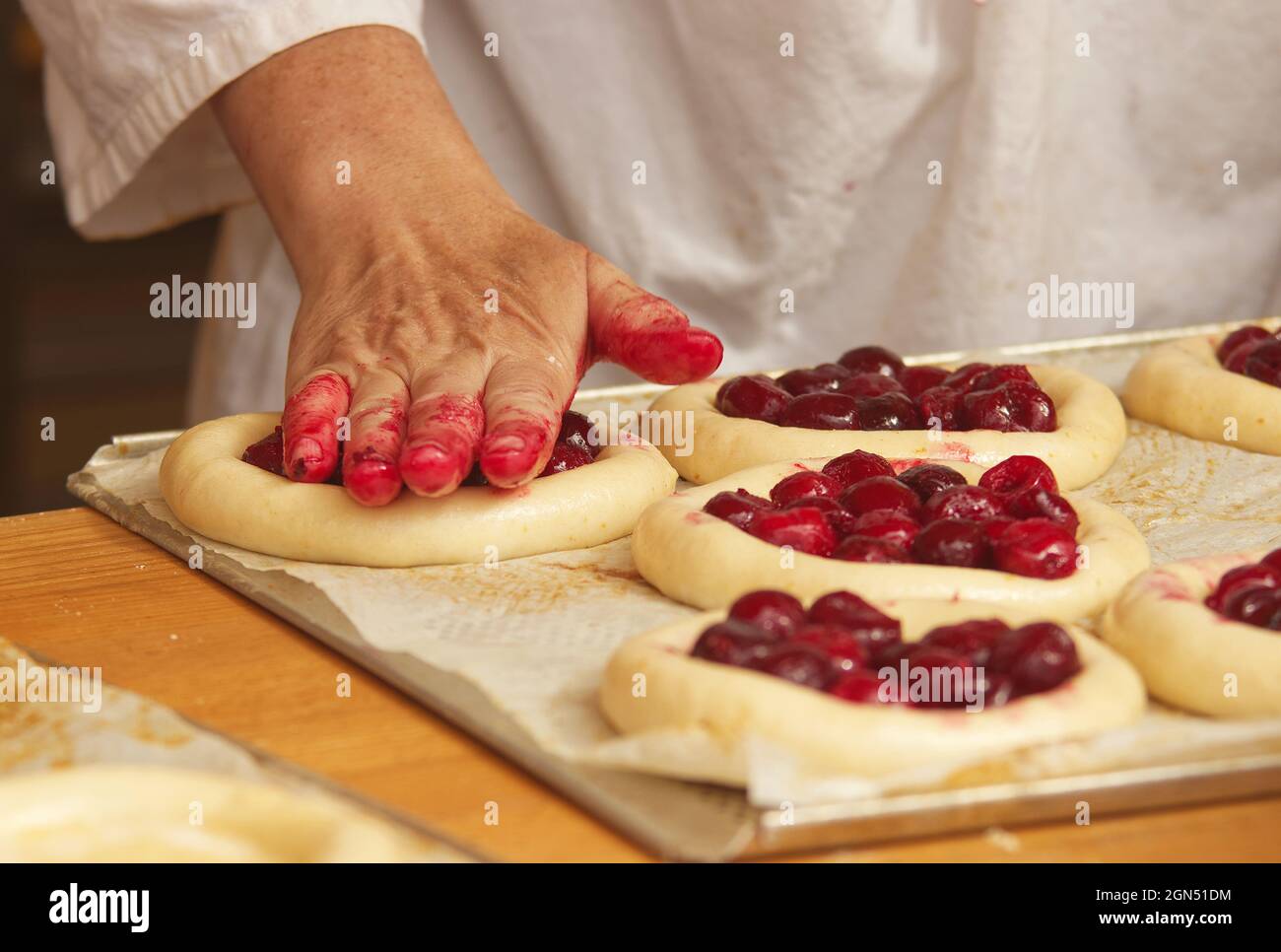 La donna nella foto sta facendo torte di frutta riempite. Mani che riempiono la pasta di lievito con fragole. Lavoro nel panificio. Foto Stock