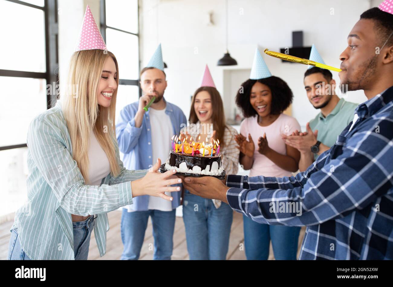 Felici amici multirazziale che danno torta di compleanno con candele alla giovane donna eccitata, avendo fresco b-giorno partito a casa Foto Stock