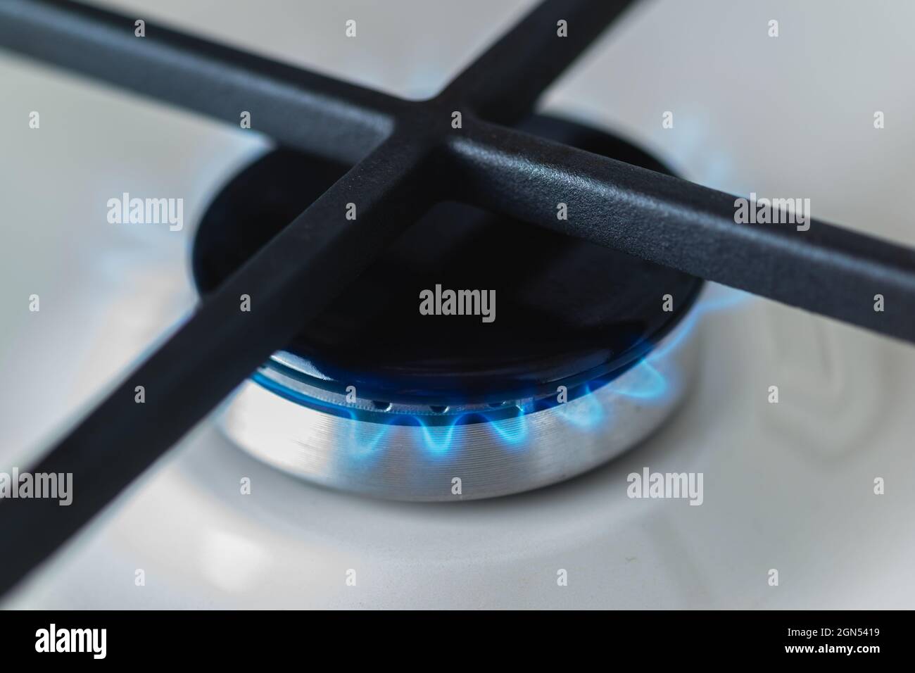 Primo piano di un bruciatore nero di una stufa a gas smaltata bianca con un fuoco blu. Griglie in ghisa per utensili da cucina Foto Stock