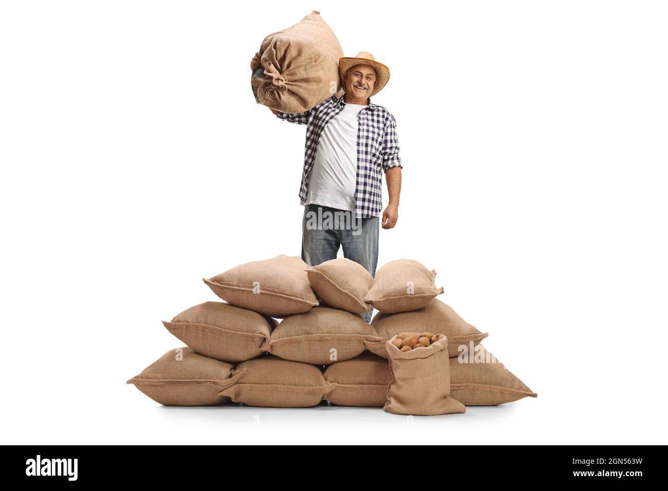 Coltivatore maturo sorridente che porta un sacco e che posa dietro sacchi con patate isolate su sfondo bianco Foto Stock