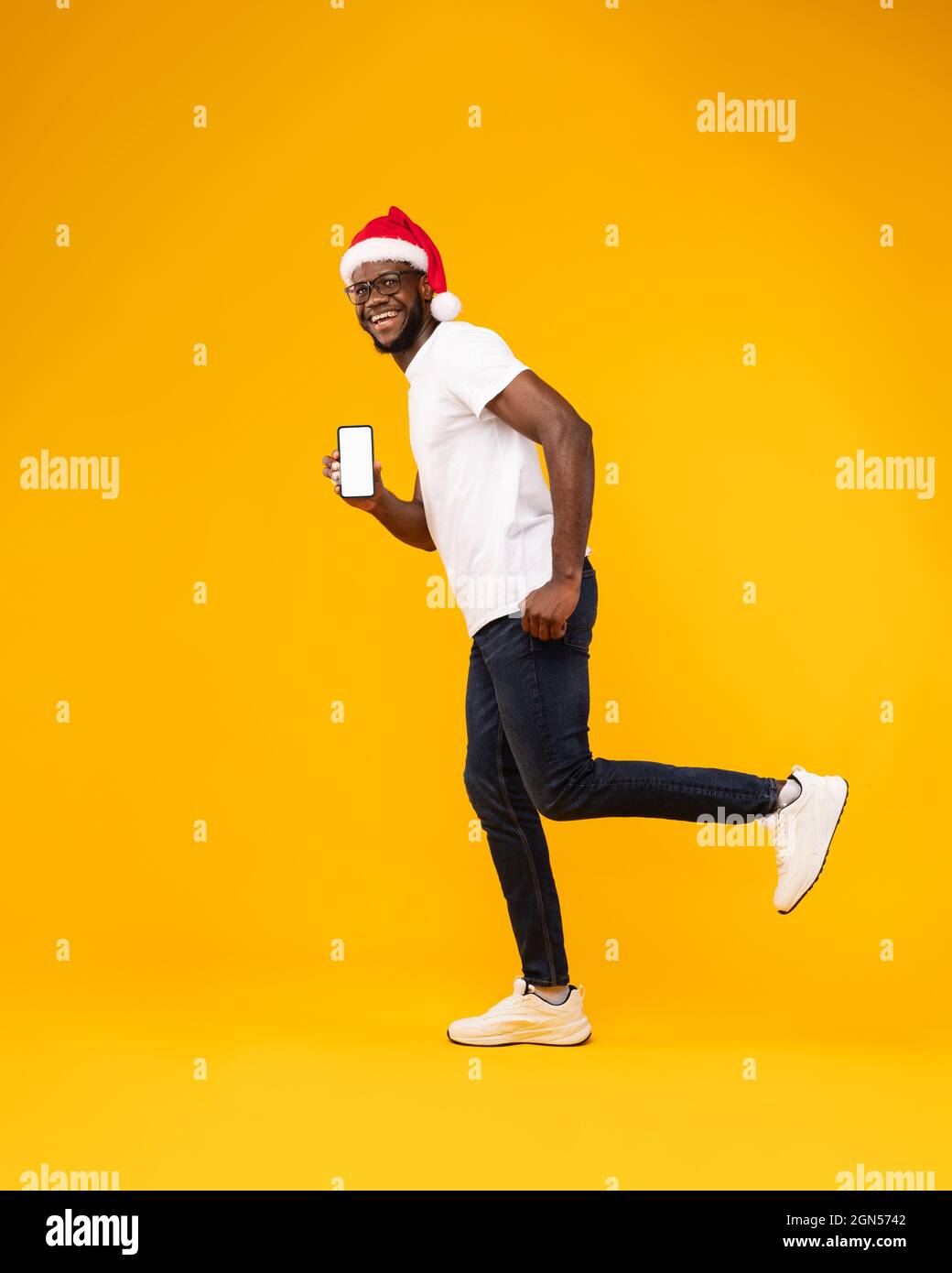Guy nero in Santa Hat che mostra la schermata Telefono, sfondo giallo Foto Stock