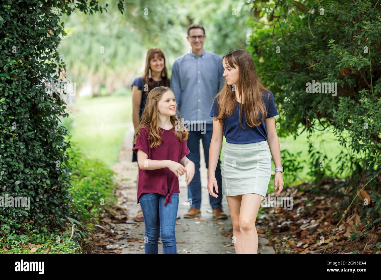 Una famiglia di una madre e di un padre e due figlie che in estate camminano nel quartiere sul marciapiede all'aperto Foto Stock