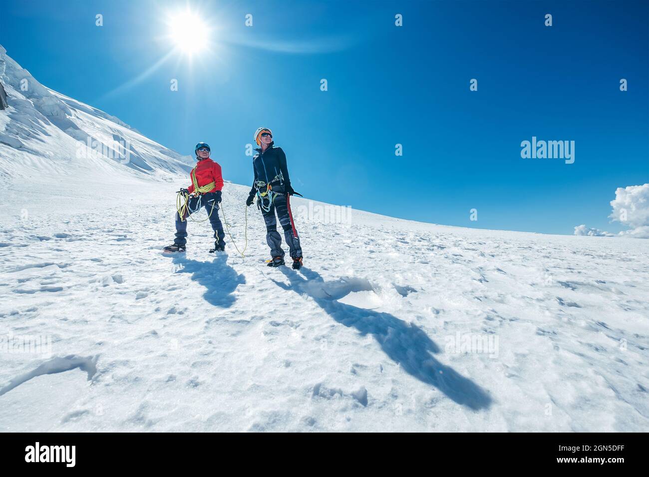Due giovani donne sorridenti Rope team discendendo Mont blanc du Tacul vertice 4248m vestiti da alpinismo con assi di ghiaccio in piedi su pendio nevoso. PE Foto Stock