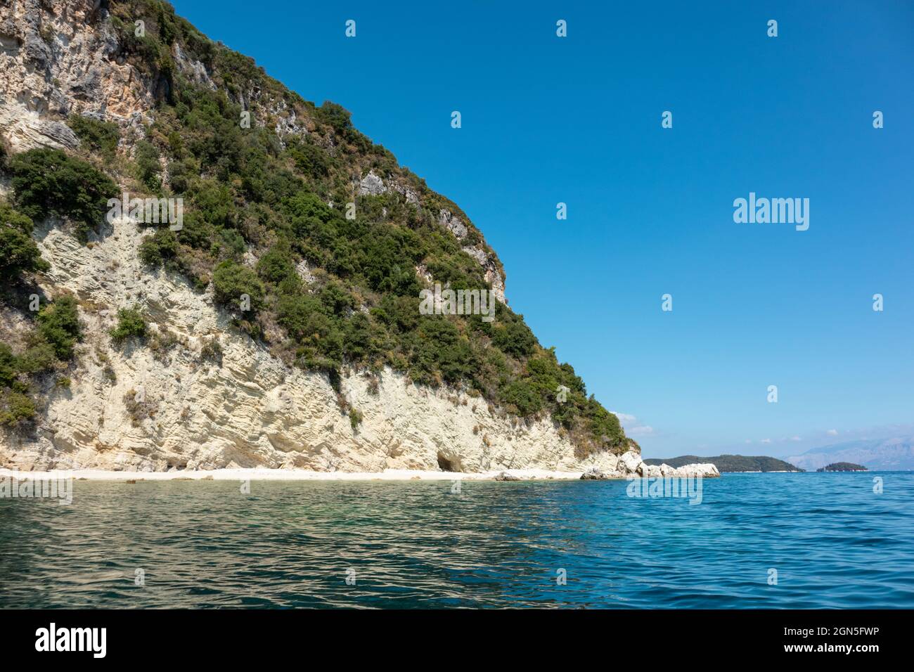 Scenica spiaggia di ciottoli bianchi nelle acque blu del Mar Ionio con scogliere verdi e cielo luminoso. Natura dell'isola di Lefkada in Grecia. Destinazione di viaggio estiva Foto Stock