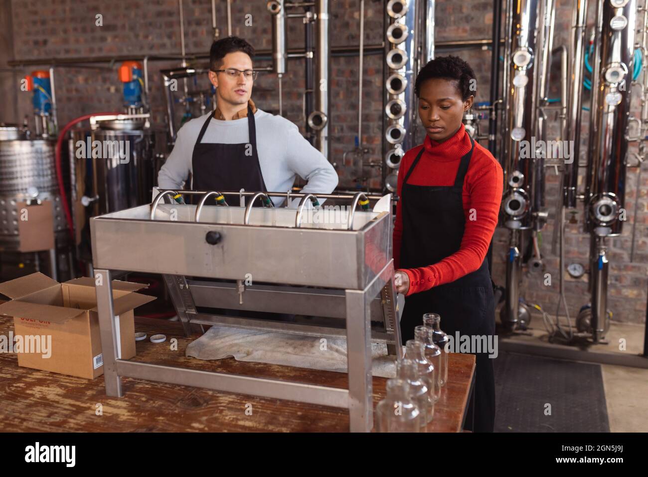 Uomo caucasico e donna afroamericana che utilizza macchinari presso la distilleria gin Foto Stock