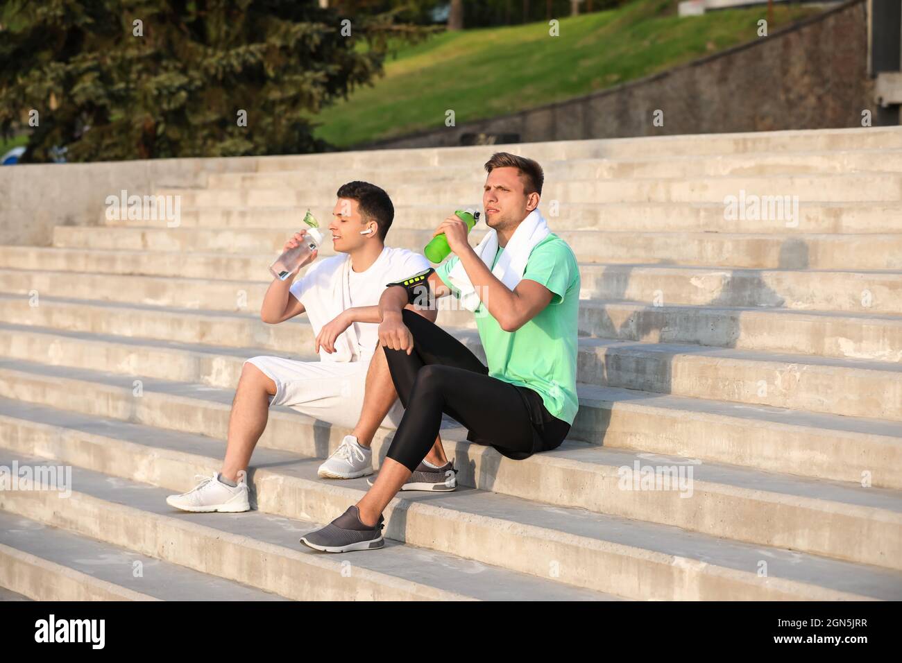 Giovani uomini sportivi che bevono acqua sulle scale all'aperto Foto Stock