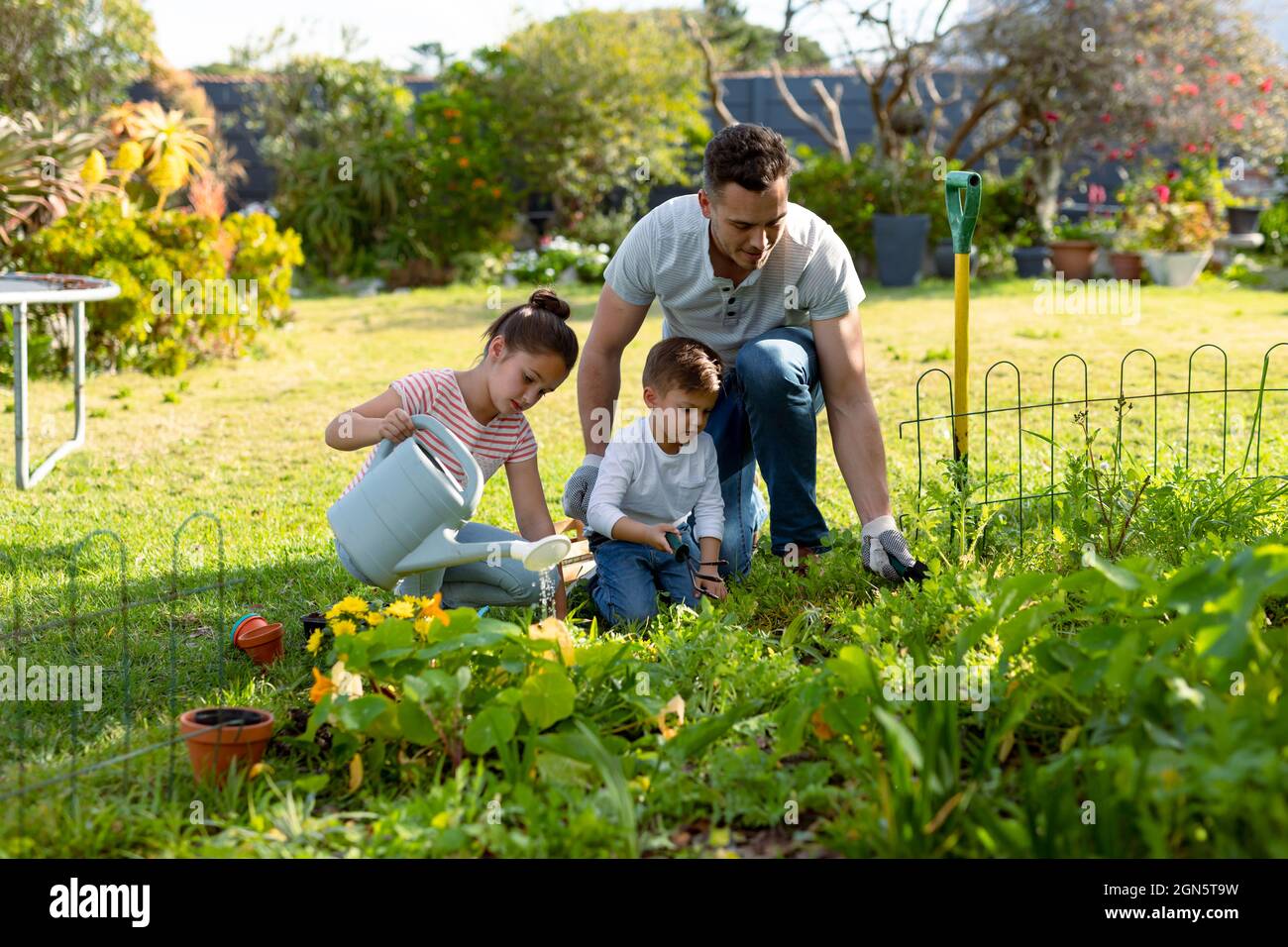 Felice padre caucasico, figlia e figlio giardinaggio e annaffiatura piante insieme Foto Stock