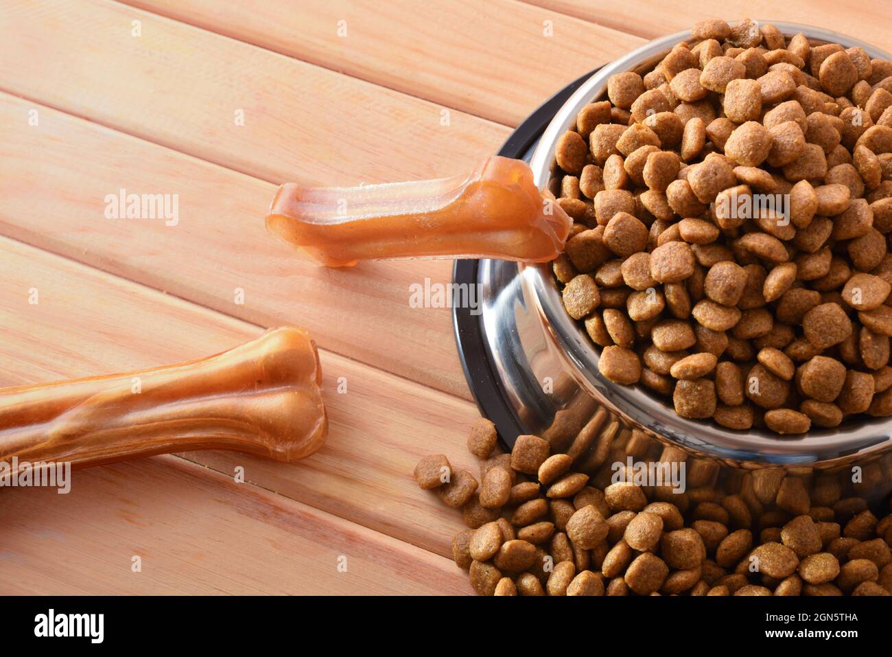Crocchette di cani in sacchi e alimentatore su tavola di legno con ossa della pelle pressate. Vista dall'alto. Composizione orizzontale. Foto Stock