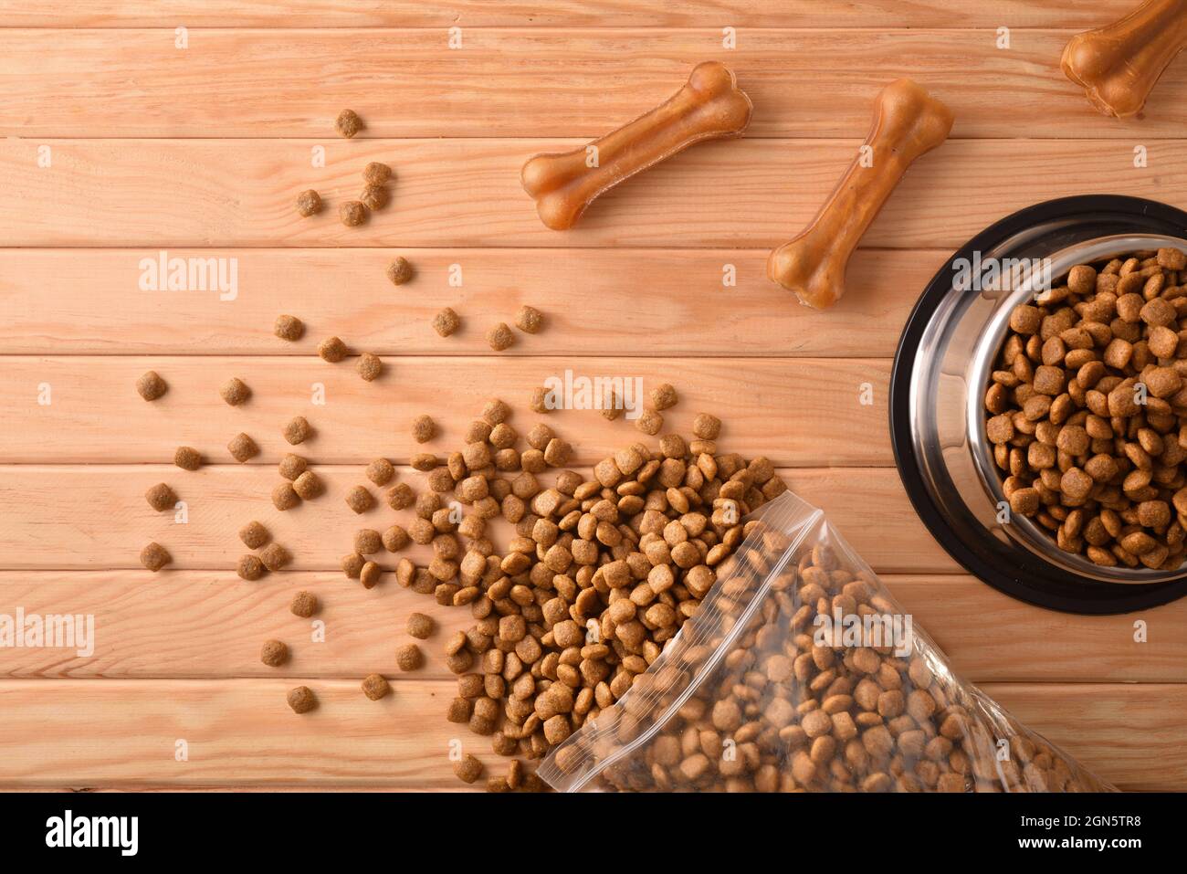 Crocchette di cani in sacchi e alimentatore su tavola di legno con ossa della pelle pressate. Vista dall'alto. Composizione orizzontale. Foto Stock