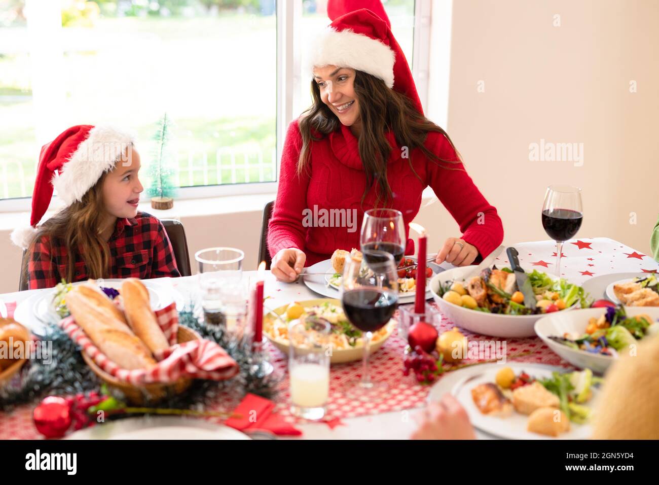 Happymother e figlia che indossano cappelli di santa seduta al tavolo di natale Foto Stock