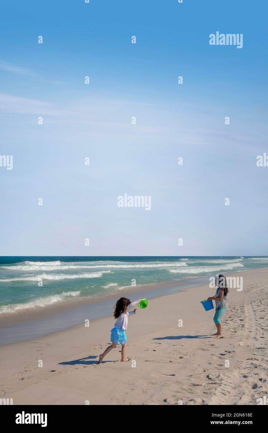 Due ragazze che giocano sulla sabbia bagnata della spiaggia con secchi di plastica Foto Stock