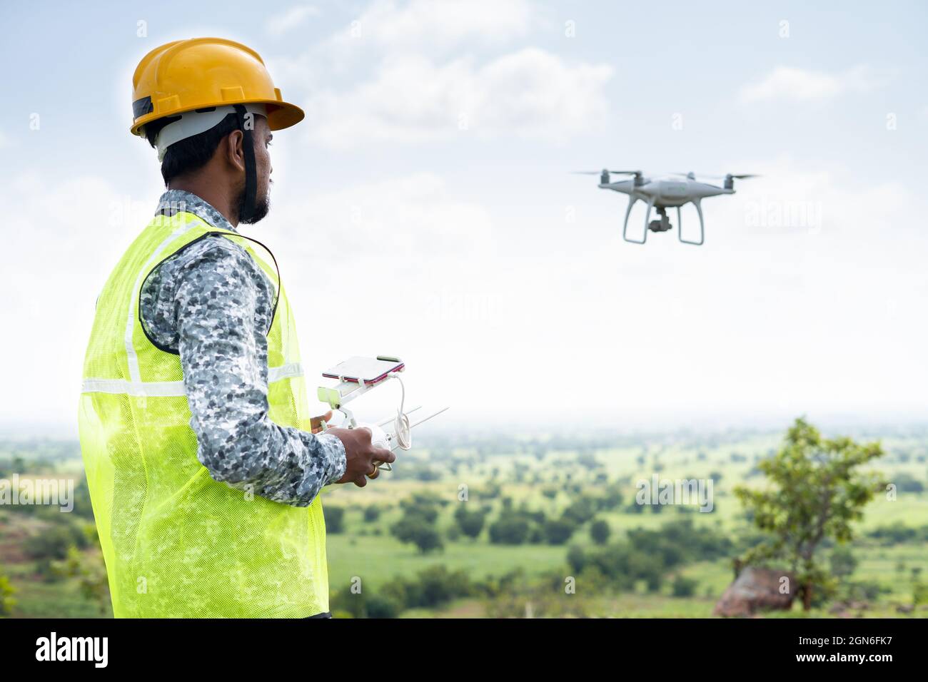 Concentratevi su pilota, pilota con drone volante con elmetto di sicurezza utilizzando il telecomando - concetto di ingegnere che fa un'indagine aerea o un'ispezione utilizzando UAV. Foto Stock