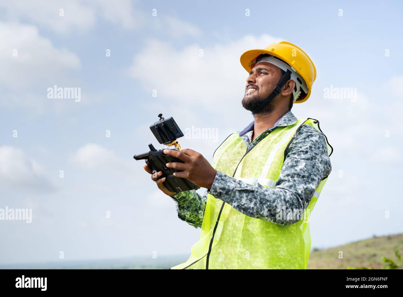 Pilota drone con elmetto di sicurezza che utilizza il drone con telecomando - concetto di ingegnere che utilizza la tecnologia dei droni per il rilevamento del terreno. Foto Stock
