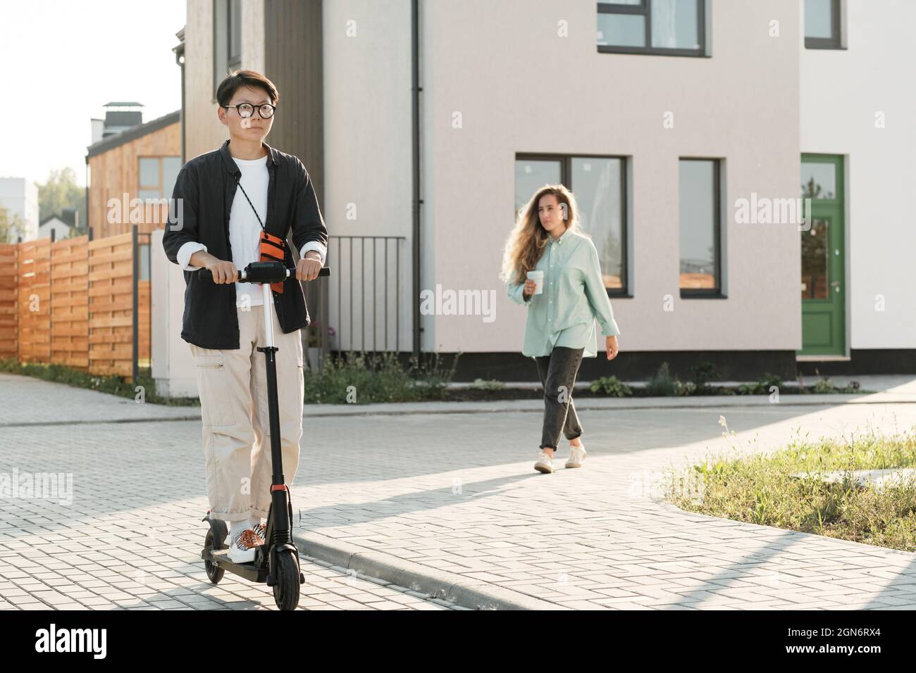 Scatto orizzontale lungo di elegante giovane donna asiatica indossando occhiali a cavallo e-scooter all'aperto in caldo sole giorno d'estate Foto Stock