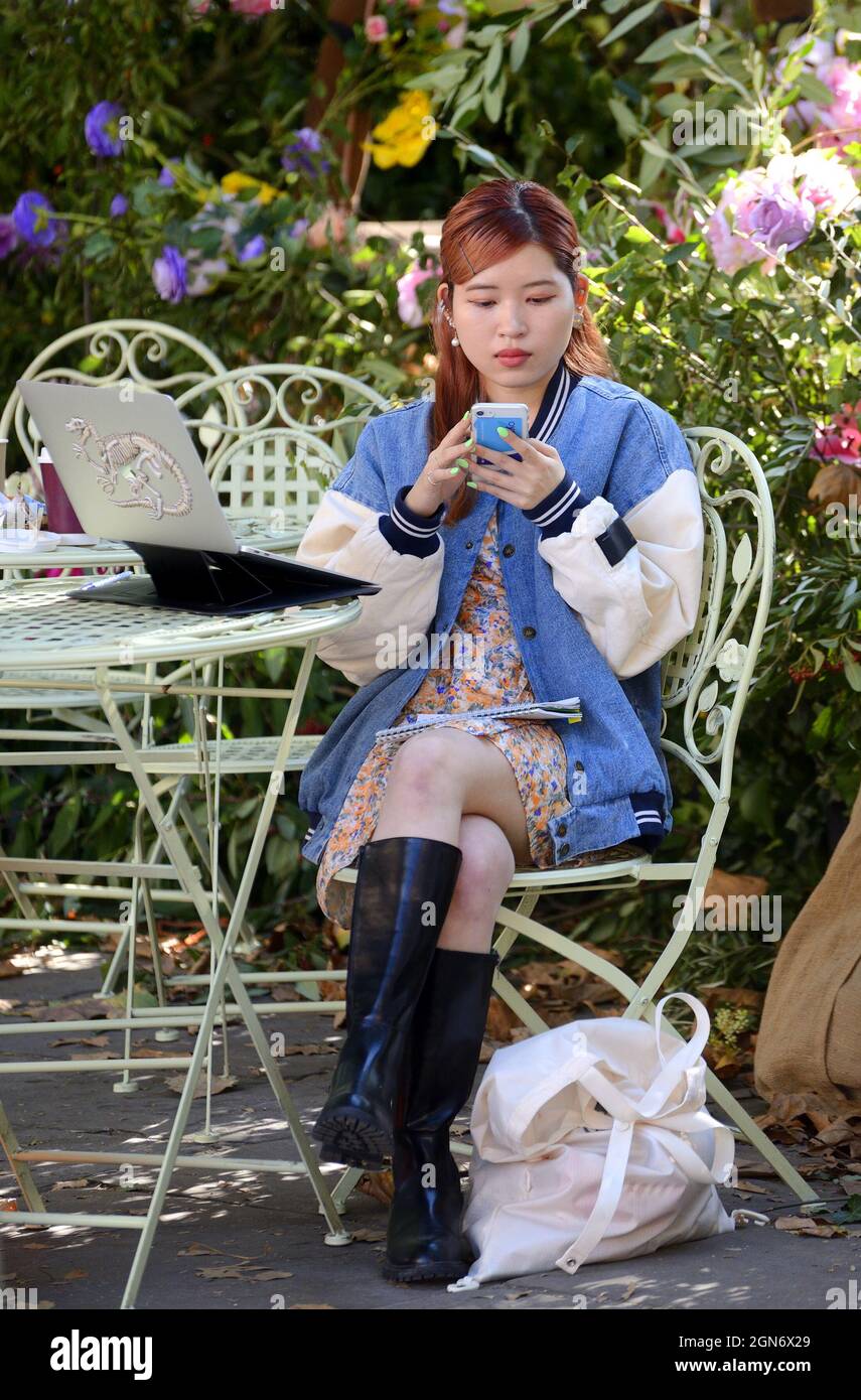 Londra, Inghilterra, Regno Unito. Giovane donna asiatica sul suo cellulare, seduto con il suo laptop, in Sloane Square, durante Chelsea in Bloom 2021 Foto Stock
