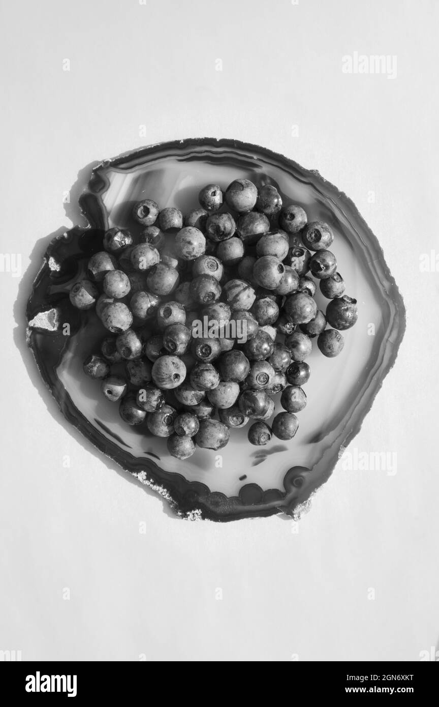 Piatto di pietra d'agata rossa e succosa, mirtilli freschi su tavola bianca. Frutti di mirtilli dolci isolati su una superficie cristallina traslucida su sfondo bianco. Spazio copia. Cibo vegetariano crudo sano Foto Stock